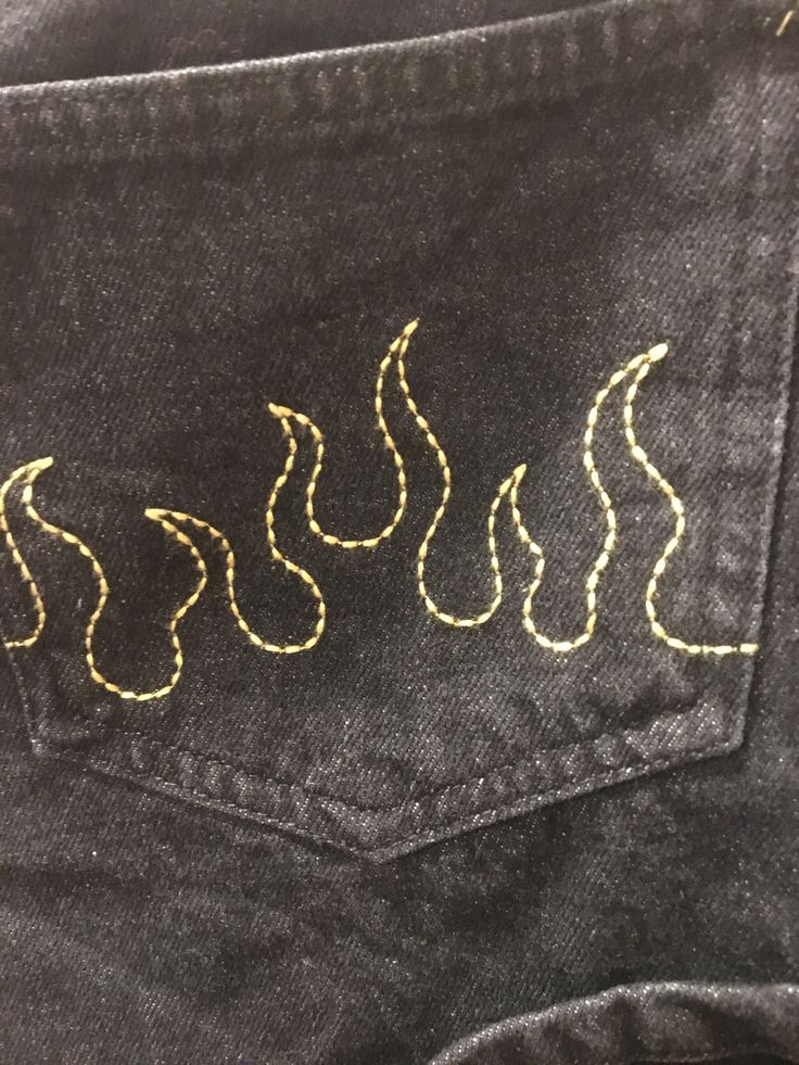 the back pocket of a pair of jeans with gold threading on it, and an embroidered design