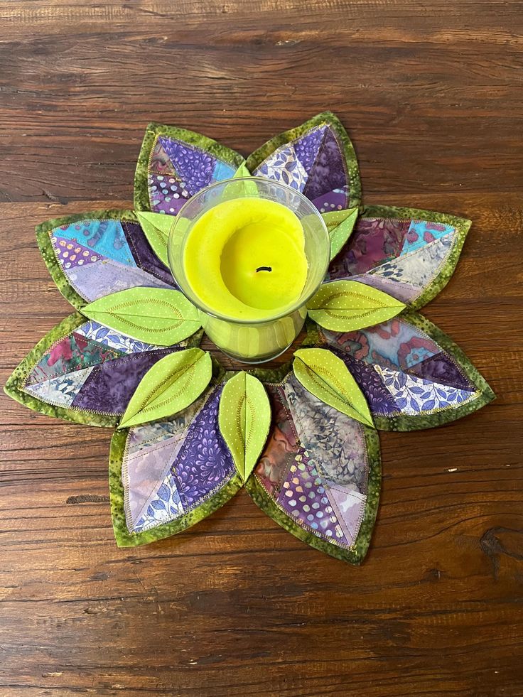 a yellow candle sitting on top of a wooden table next to a green leafy flower