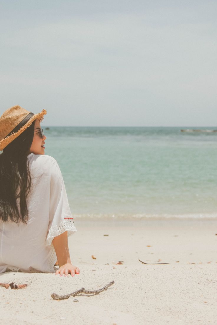 a woman sitting on the beach looking out at the ocean