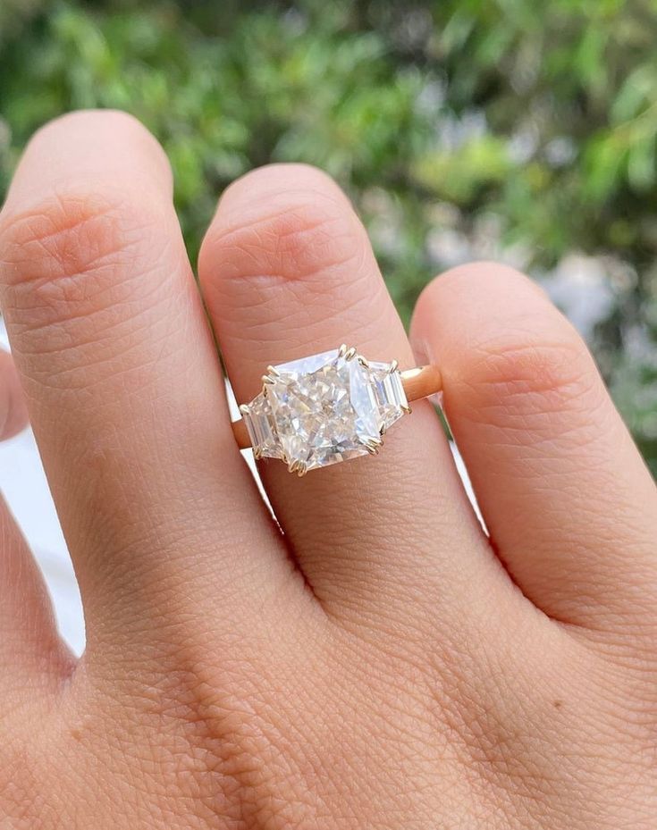 a woman's hand holding an engagement ring with a diamond in the middle and two diamonds on each side