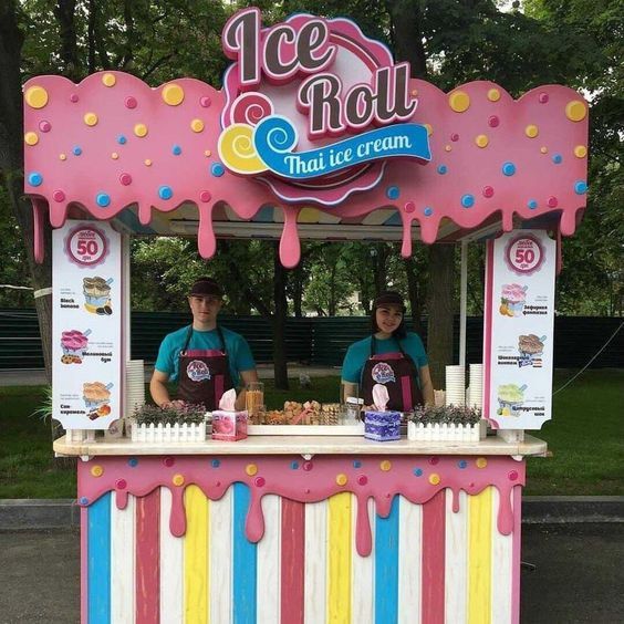 two people standing behind a colorful ice cream stand