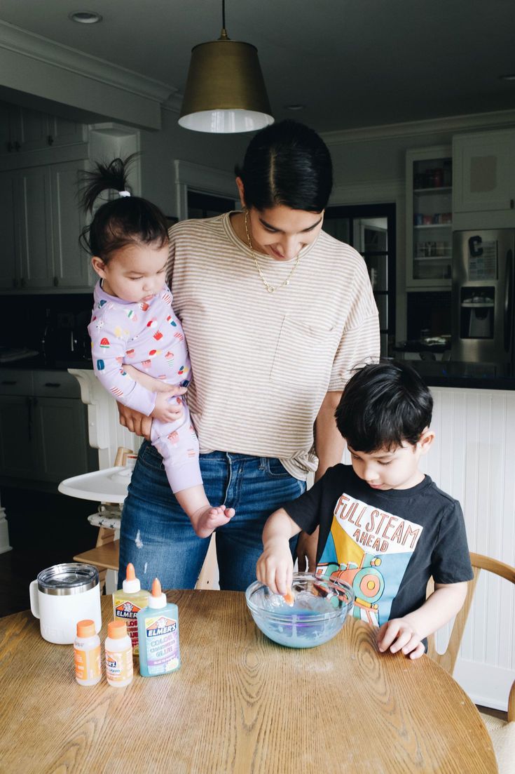 a woman standing next to a little boy at a table with food in a bowl