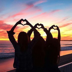 three girls making heart shapes with their hands on the beach at sunset or sunrise time