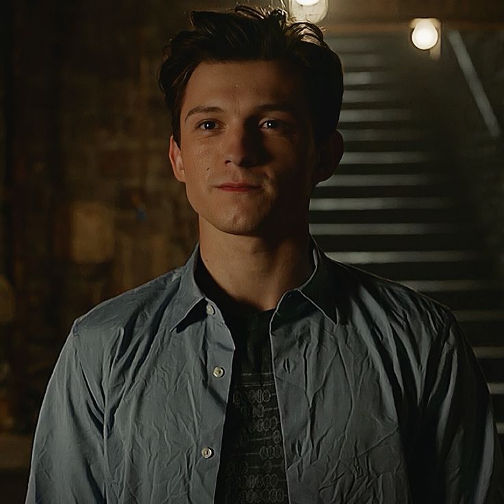 a young man wearing a blue shirt and tie standing in front of some stairs at night