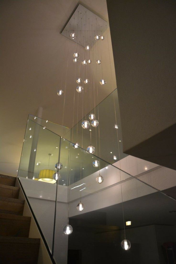 a modern chandelier hanging from the ceiling in a room with stairs and windows