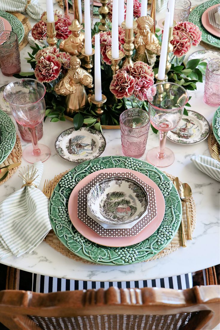 the table is set with pink and green plates, silverware, and candlesticks