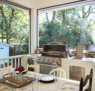 a kitchen with an outdoor grill and dining table set for four in front of large windows