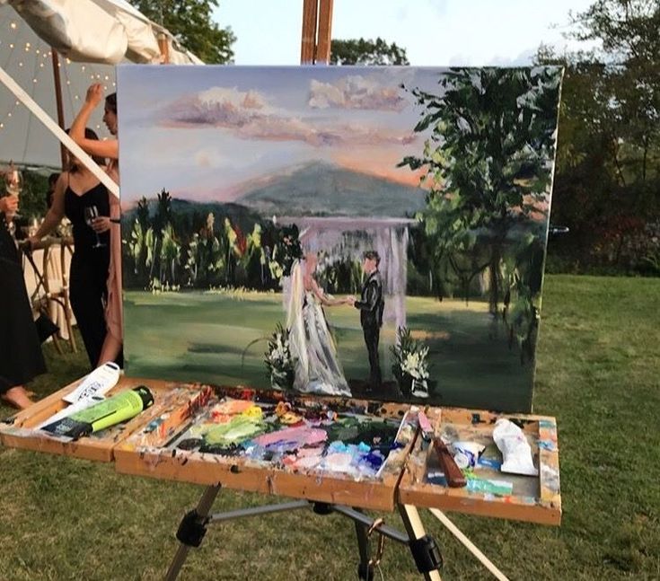 a painting is being displayed on a easel in the grass with people looking at it