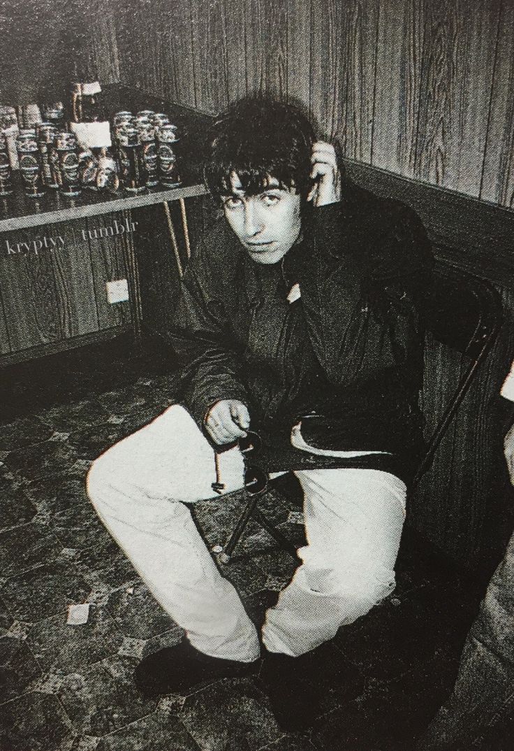 black and white photograph of young man sitting on chair in room with shelves full of jars