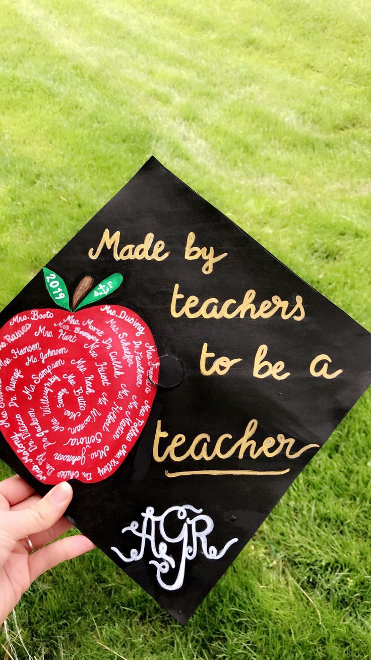 a hand holding up a black graduation cap with an apple on it that says made by teachers to be a teacher