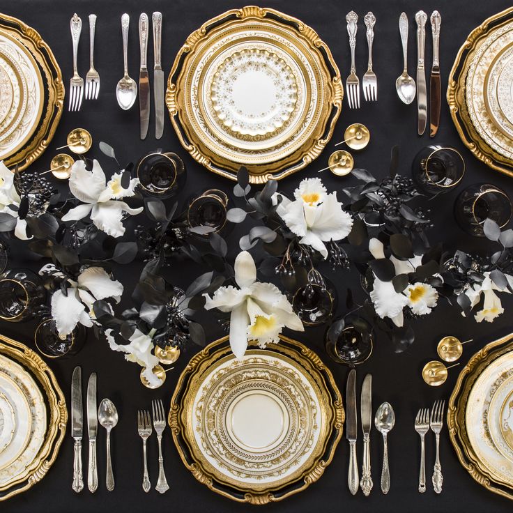 the table is set with gold and white plates, silverware, and orchids