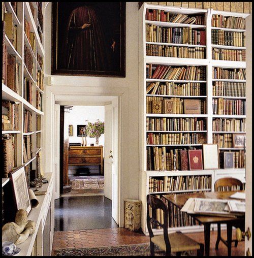 a room filled with lots of books next to a table and chairs in front of a painting