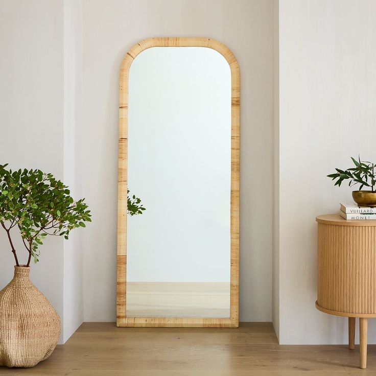 a mirror sitting on top of a wooden table next to a vase filled with plants