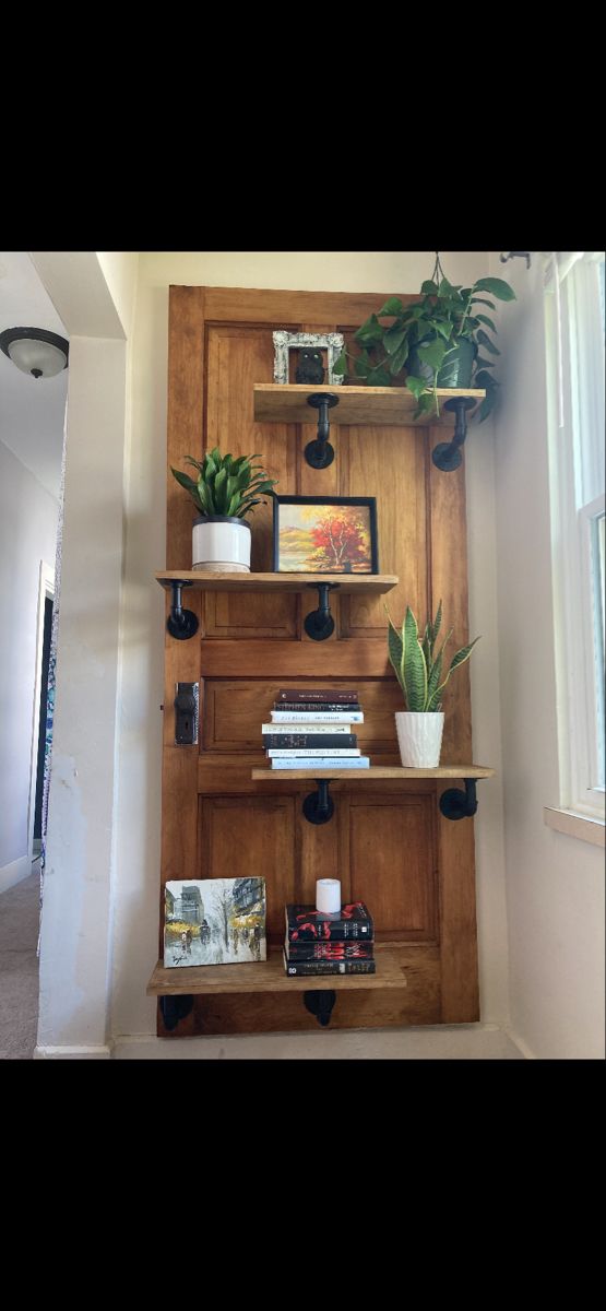 a wooden shelf with books and plants on it in a room next to a window