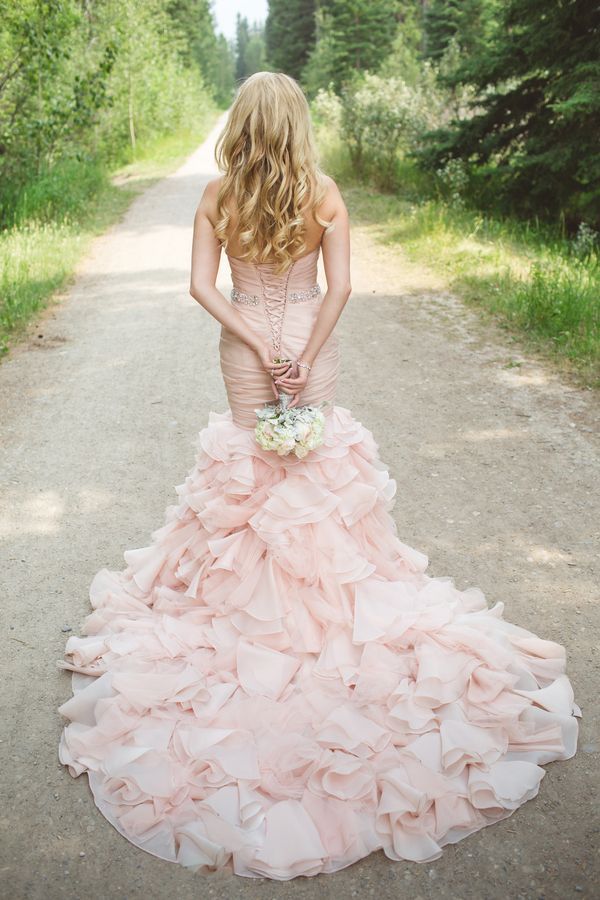 a woman in a pink wedding dress standing on a dirt road with trees behind her