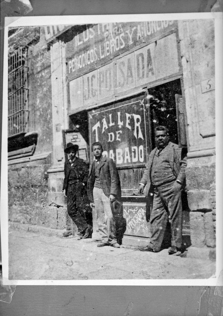 three men standing in front of a building with a sign that reads taller de oro