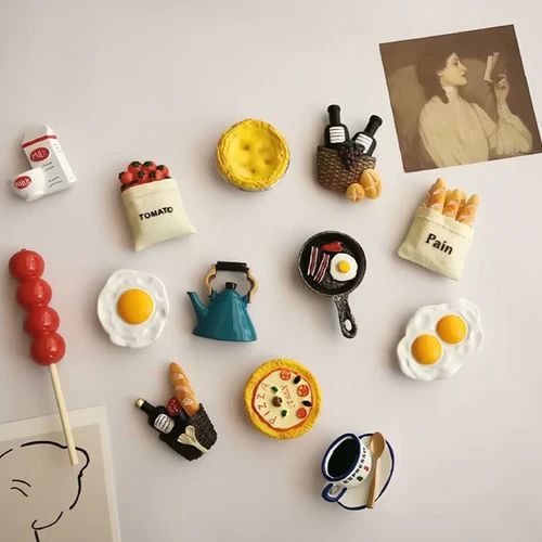 a refrigerator with magnets and food on it's side, including an egg, toaster, coffee cup, teapot, hot dog, cookie, and other items