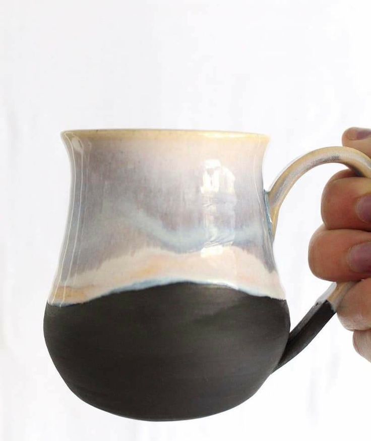 a hand holding a black and white ceramic coffee mug with liquid pouring out of it