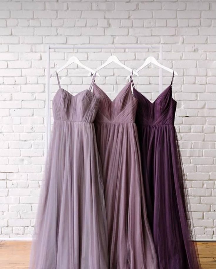 three bridesmaid dresses hanging on a rack in front of a white brick wall