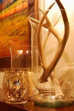 two glass vases with antlers in them sitting on a table next to a painting