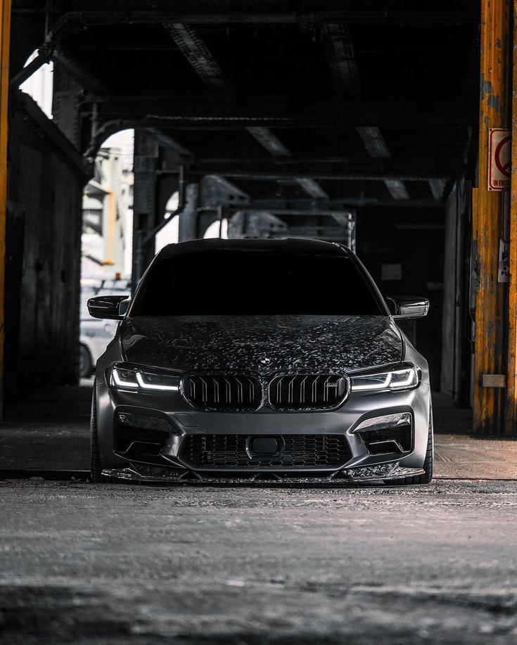 the front end of a silver car parked in a parking garage with graffiti on it