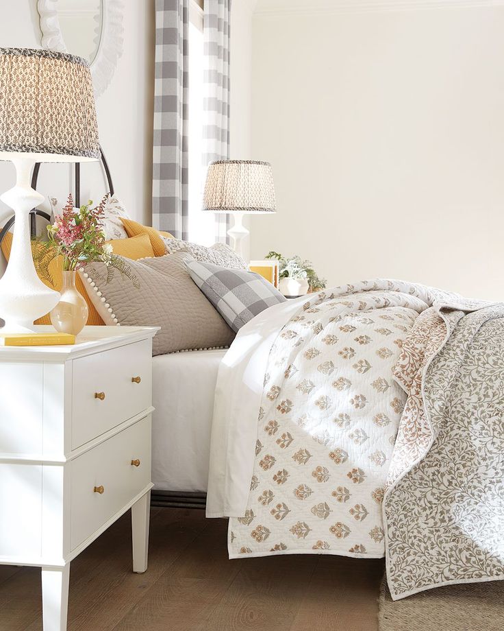 a white bed sitting next to a window in a bedroom with plaid curtains and pillows