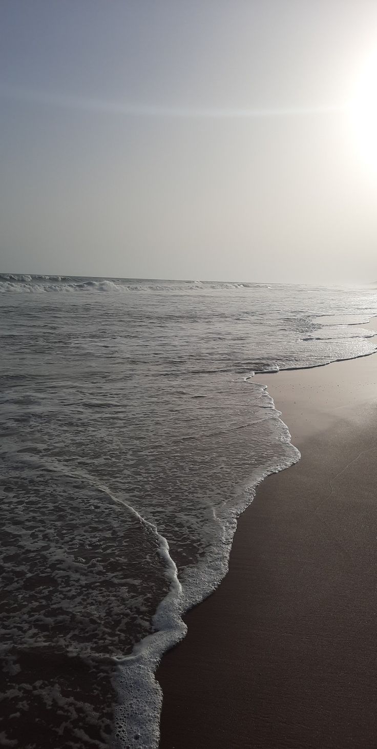 the sun is shining over the water at the shore line as waves roll in on the beach