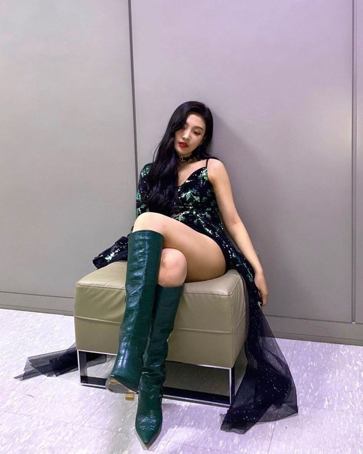 a woman sitting on top of a chair wearing green boots and a black dress with sequins