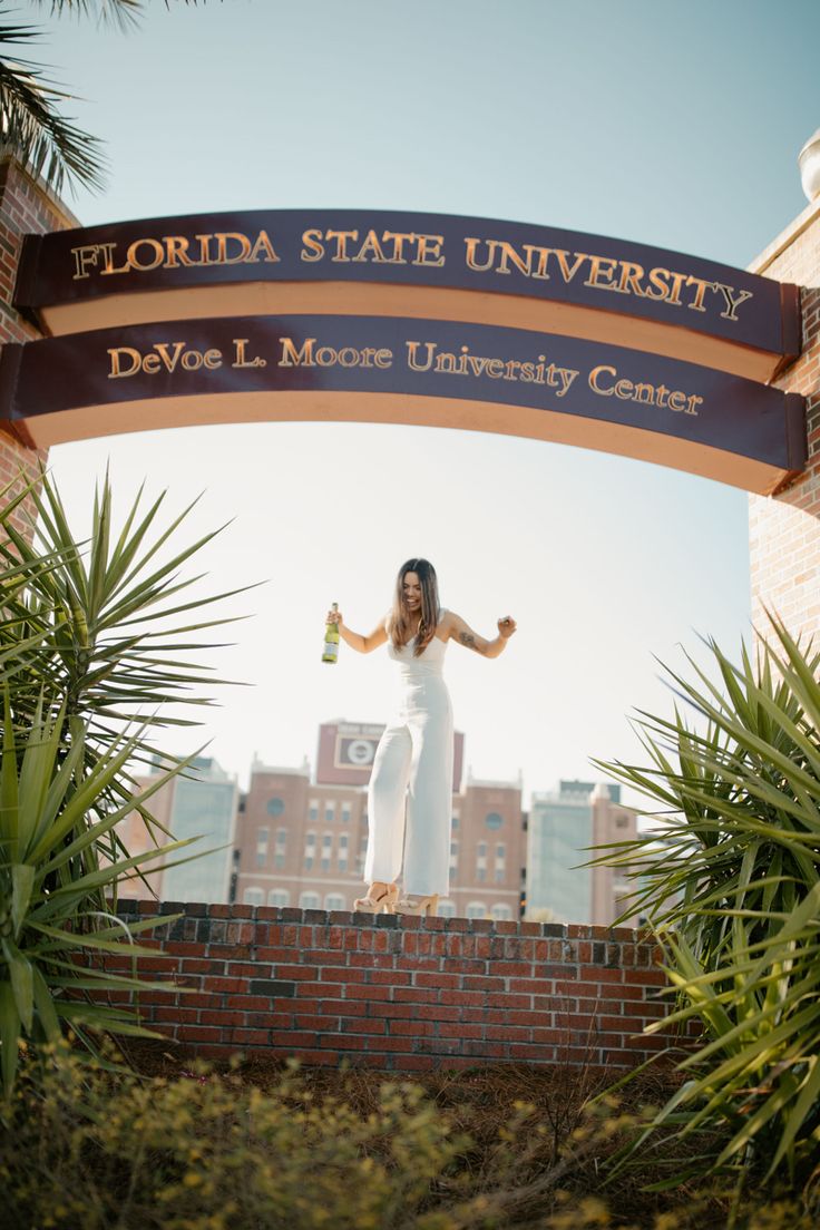 a woman standing on top of a brick wall in front of a florida state university sign