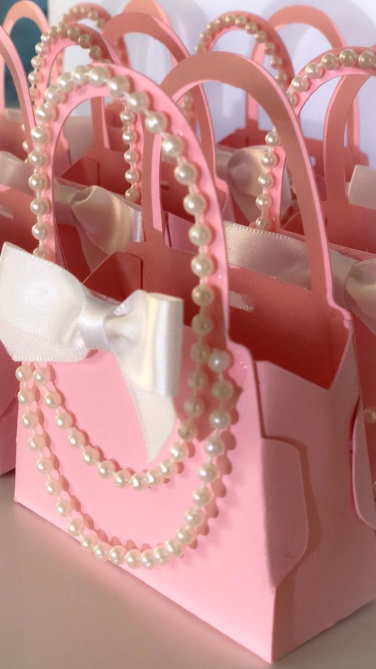 pink and white bags with pearls on the handles are sitting on a table next to each other