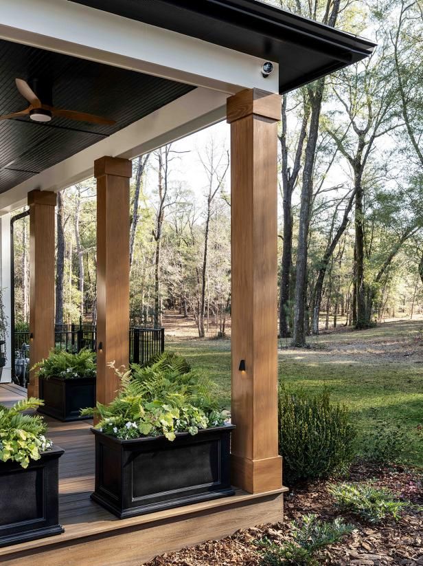 two black planters on the front porch with green plants in them and an awning