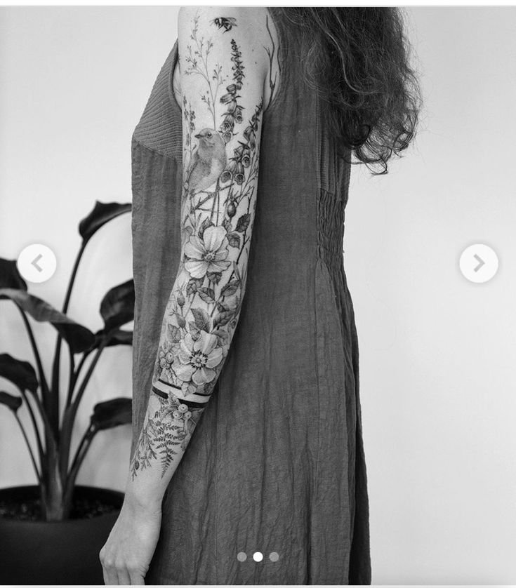 a woman with tattoos on her arm standing in front of a potted plant