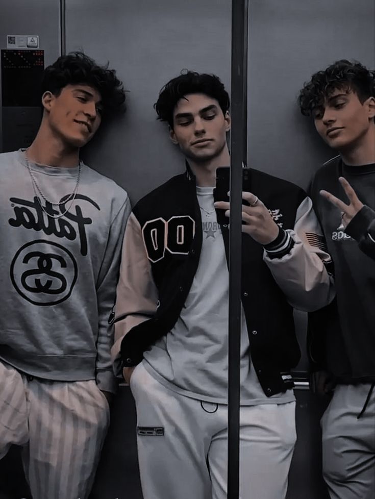 three young men standing next to each other in front of a wall holding cell phones