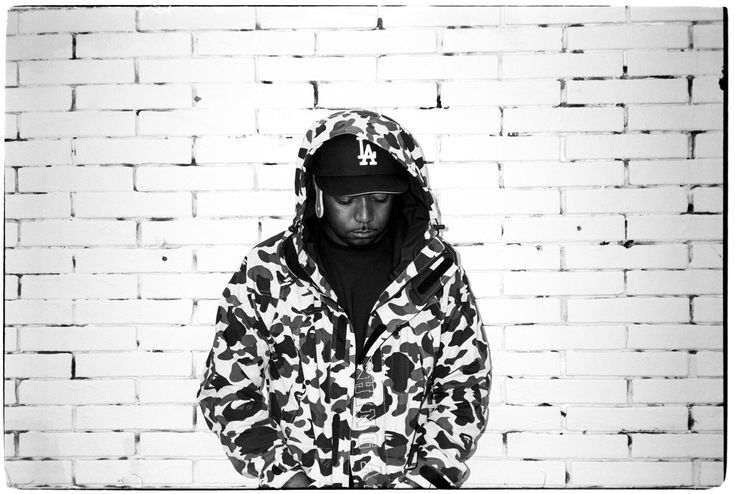 a man standing in front of a brick wall wearing a hoodie and holding a skateboard