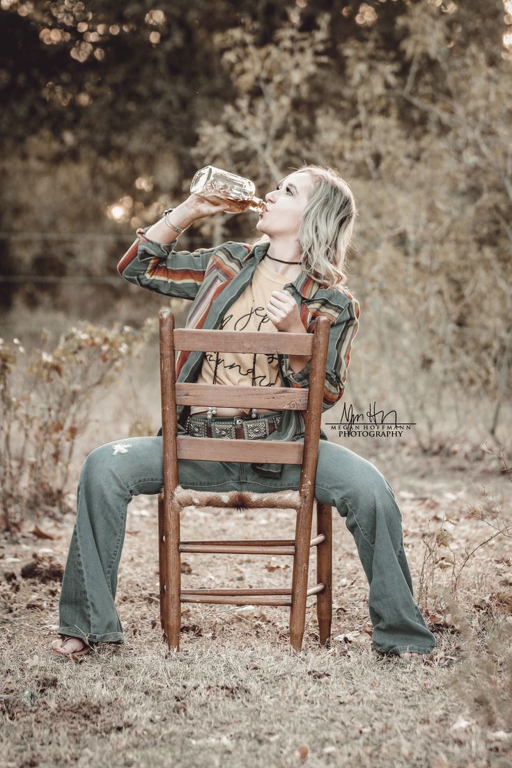 a woman sitting in a wooden chair drinking from a bottle while looking up into the sky