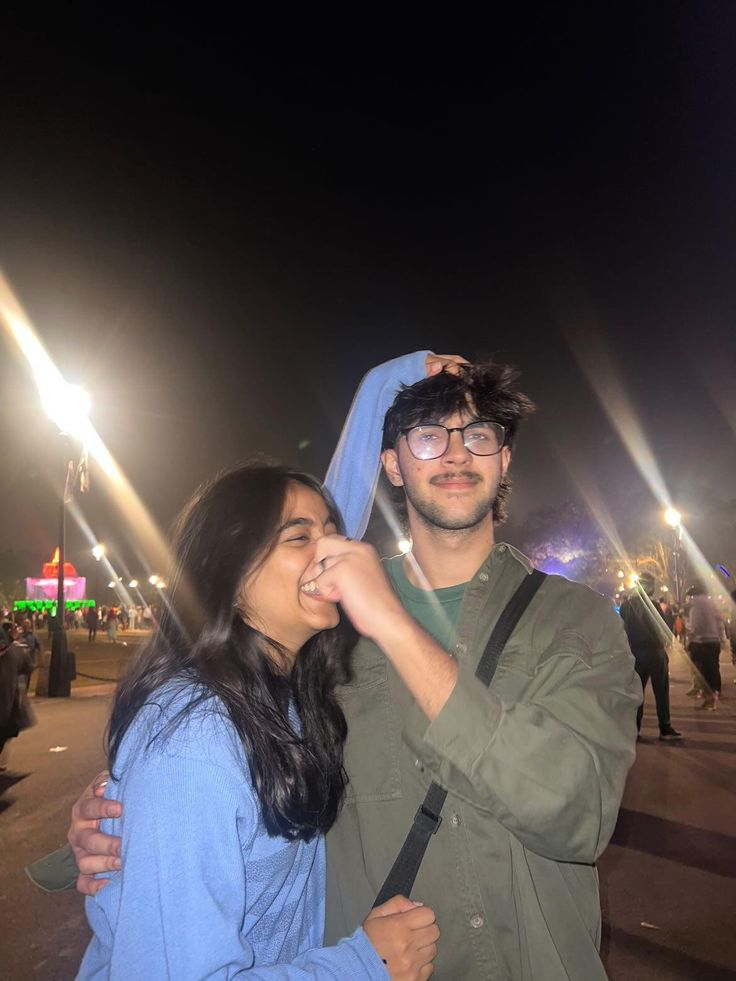 a man and woman standing next to each other in front of street lights at night