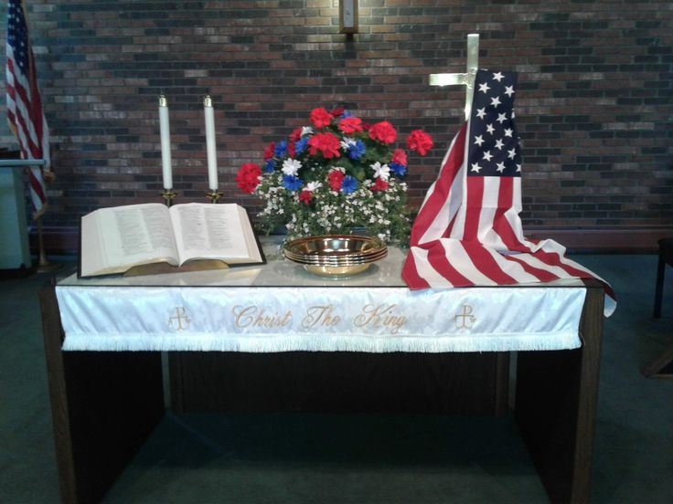 an american flag and flowers on a table in front of a brick wall with a lit candle