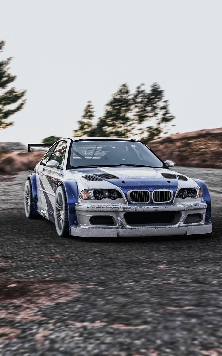 a blue and white car driving down a dirt road next to some trees in the background