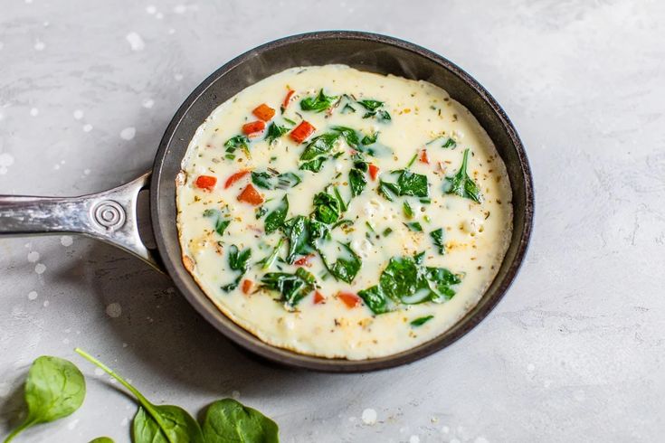 a pan filled with cheese and spinach on top of a table next to some leaves