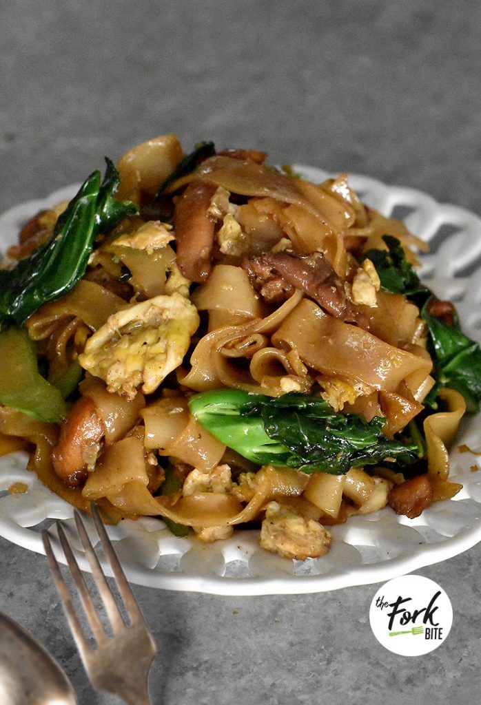 a white plate topped with pasta and veggies next to a fork on a table