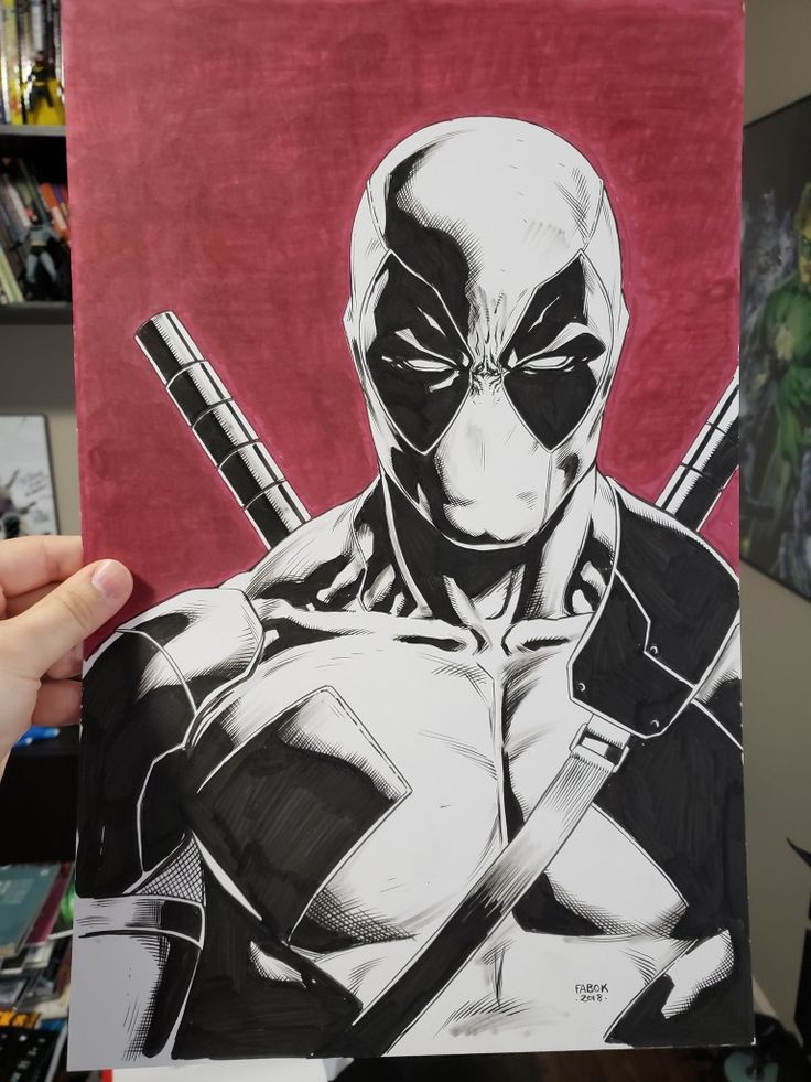 a hand holding up a drawing of a deadpool with two swords in his hands