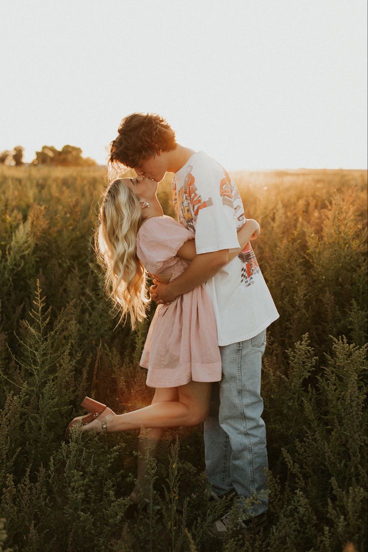 a man and woman kissing in the middle of a field with tall grass at sunset