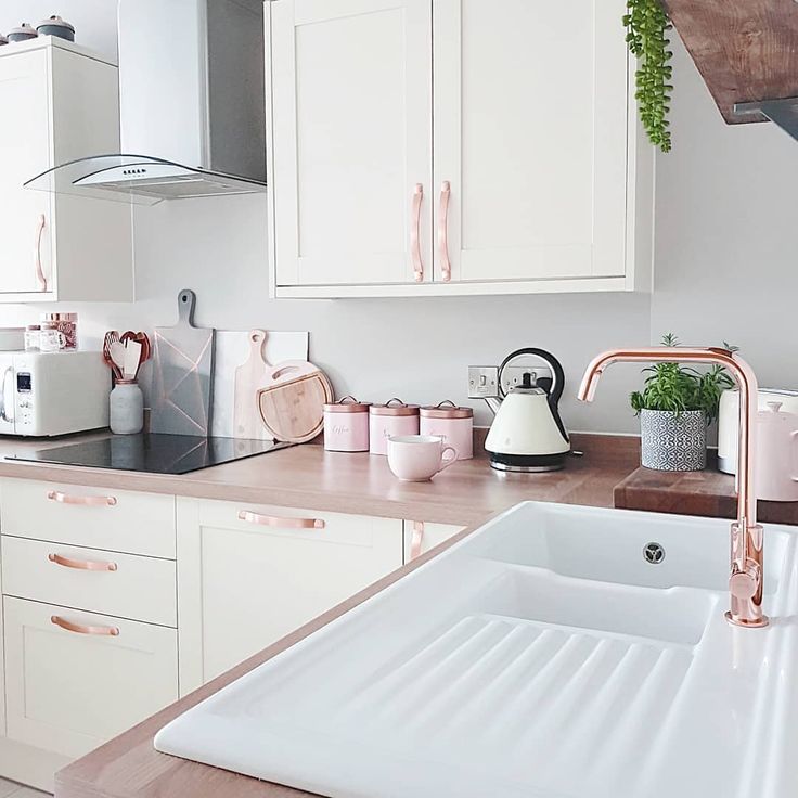 a kitchen with white cabinets and pink accessories on the counter top, along with a copper faucet