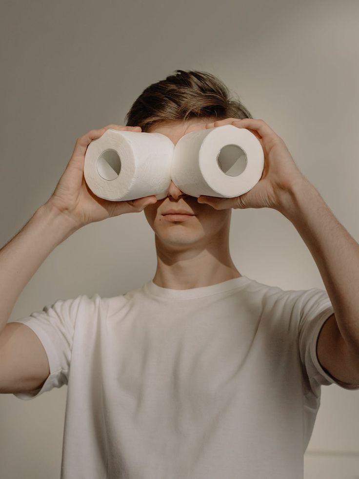 a man holding two rolls of toilet paper in front of his eyes while looking through them