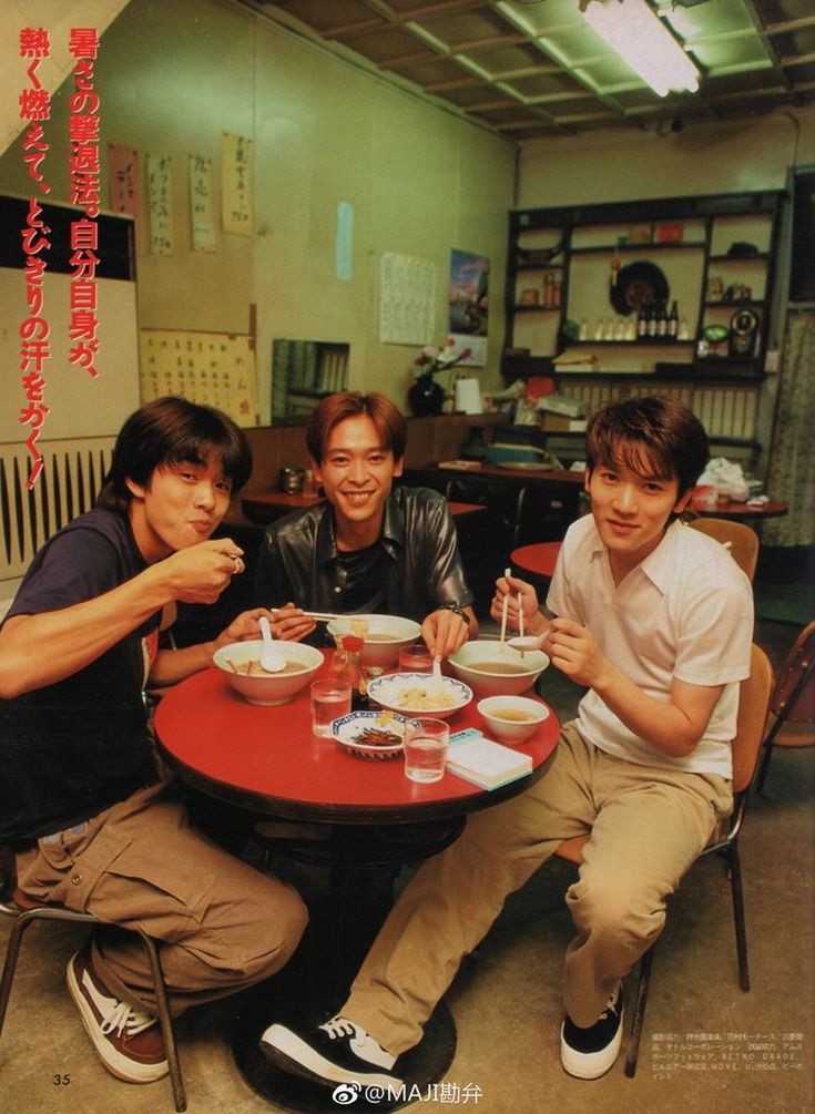 three young men sitting at a table with bowls of food in front of them,