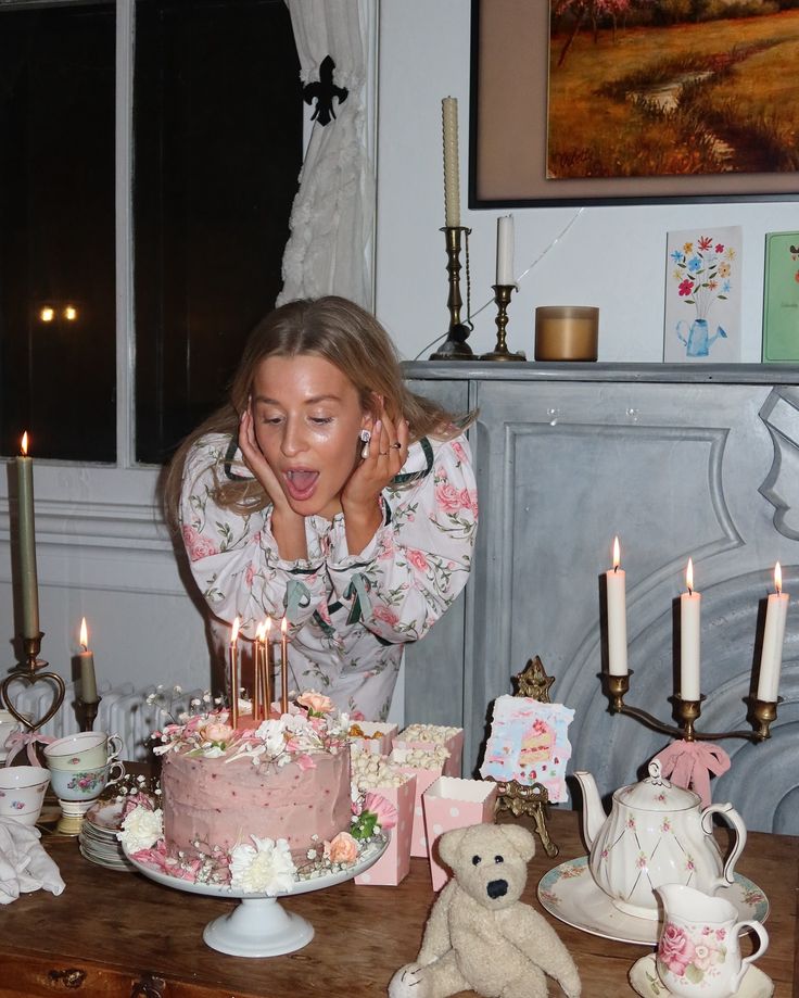 a woman blowing out candles on a cake with teddy bears and teacups around it