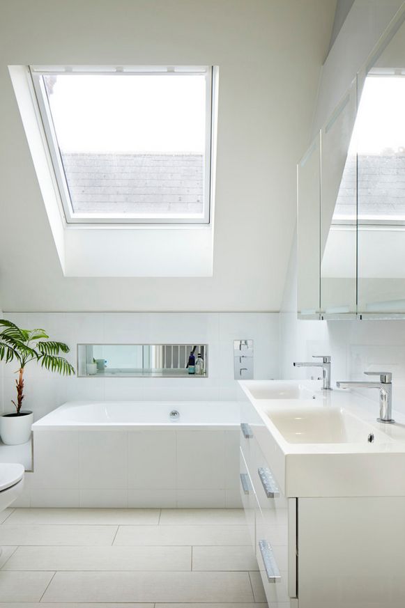 a white bathroom with two skylights above the bathtub and sink, along with a potted plant