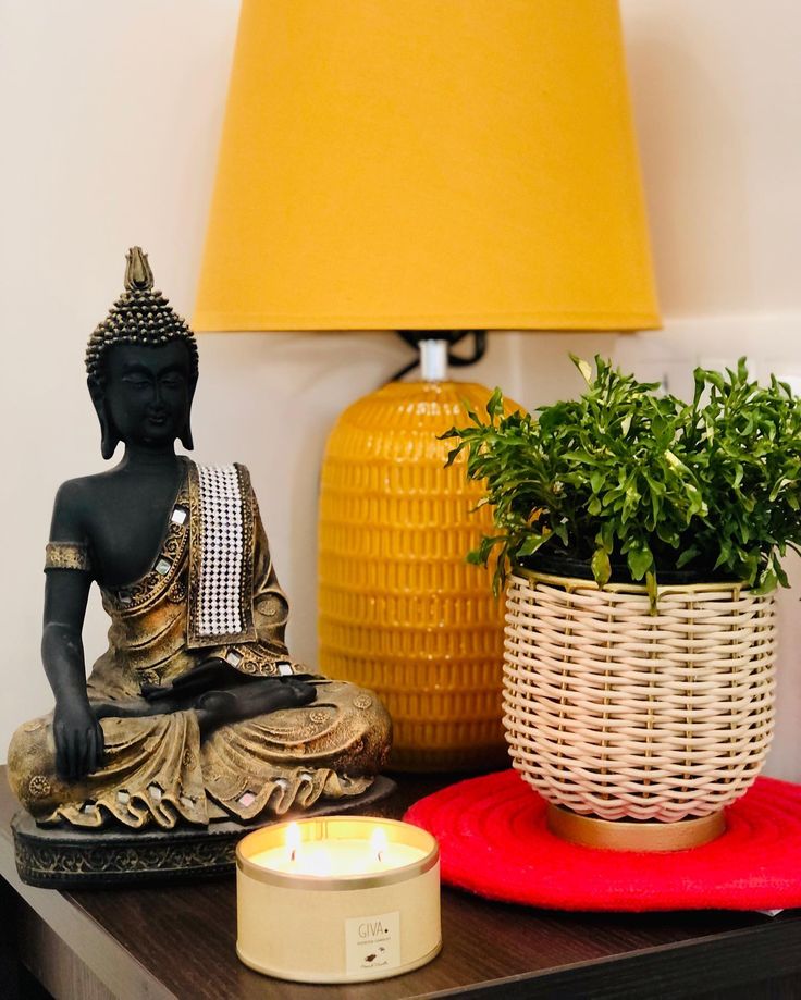 a buddha statue sitting on top of a wooden table next to a yellow lamp and potted plant