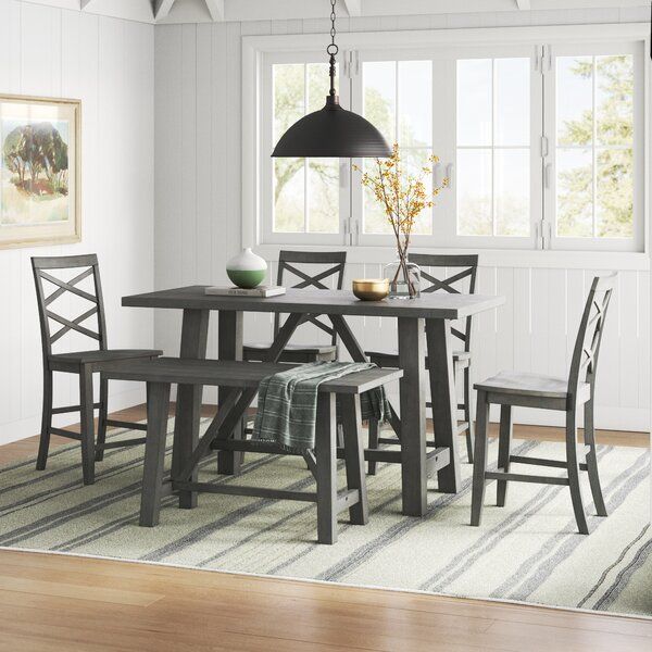 a dining room table with four chairs and a bench in front of a window on a rug