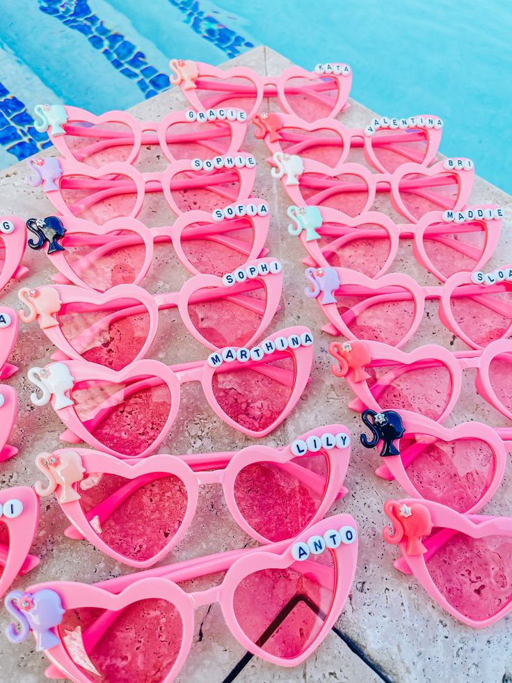 many pink sunglasses are lined up on the side of a swimming pool with name tags attached to them